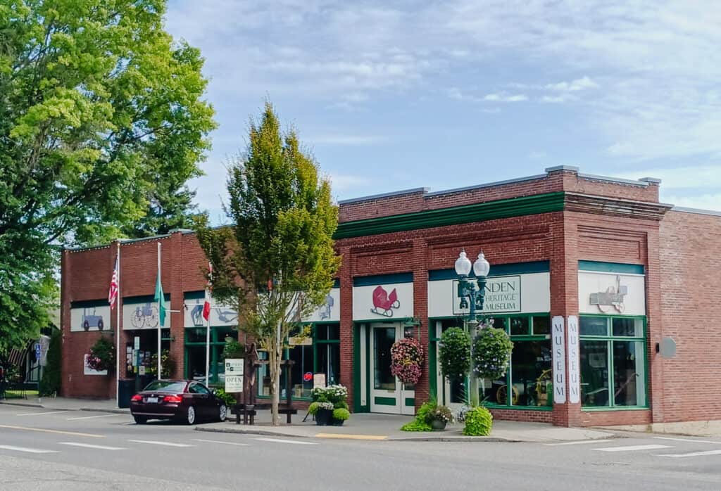 red brick building wtih green trim and illustrations of vintage vehicles, trees, flags and streetlamps in foreground, lynden heritage museum