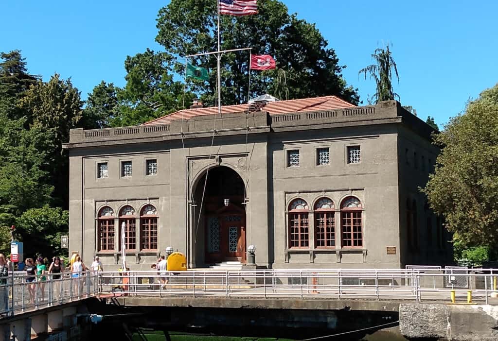 grey 2 story building along locks, large arched entryway, American flag on top and tree and blue sky in background