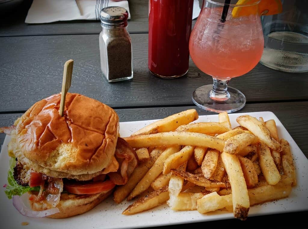 Burger and french fries on a white rectangular plate. Pink cocktail and a pepper shaker in the background.