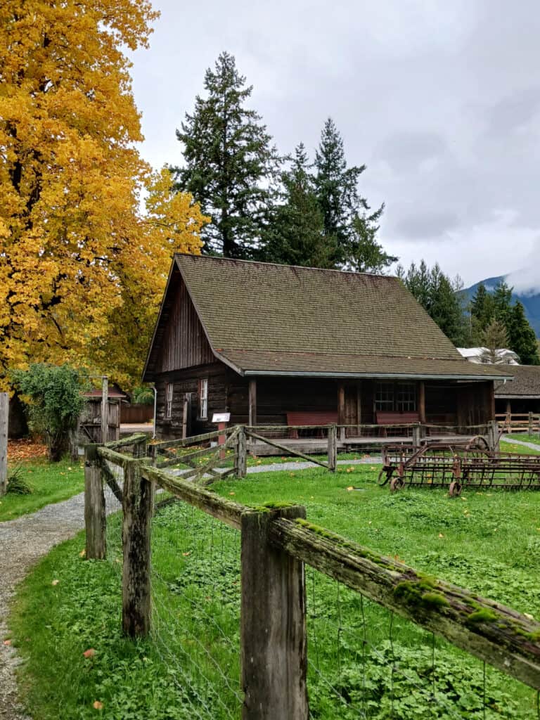 log cabin with fenced field and old farm implement in the field. Tree with yellow leaves.