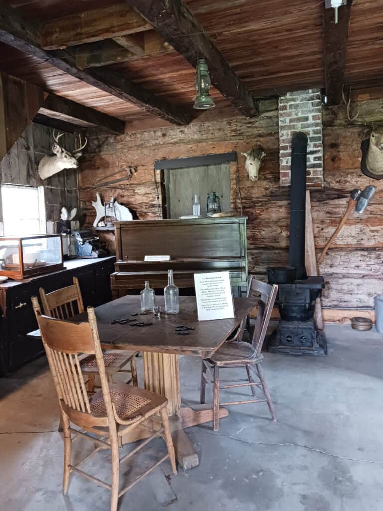 interior of saloon at Cashmere pioneer village with piano and woodstove in background and table with chairs in foreground, empty glass bottles on table