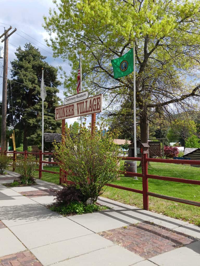 sign with sidewalk in foreground and trees in background; Cashmere Museum and Pioneer Village